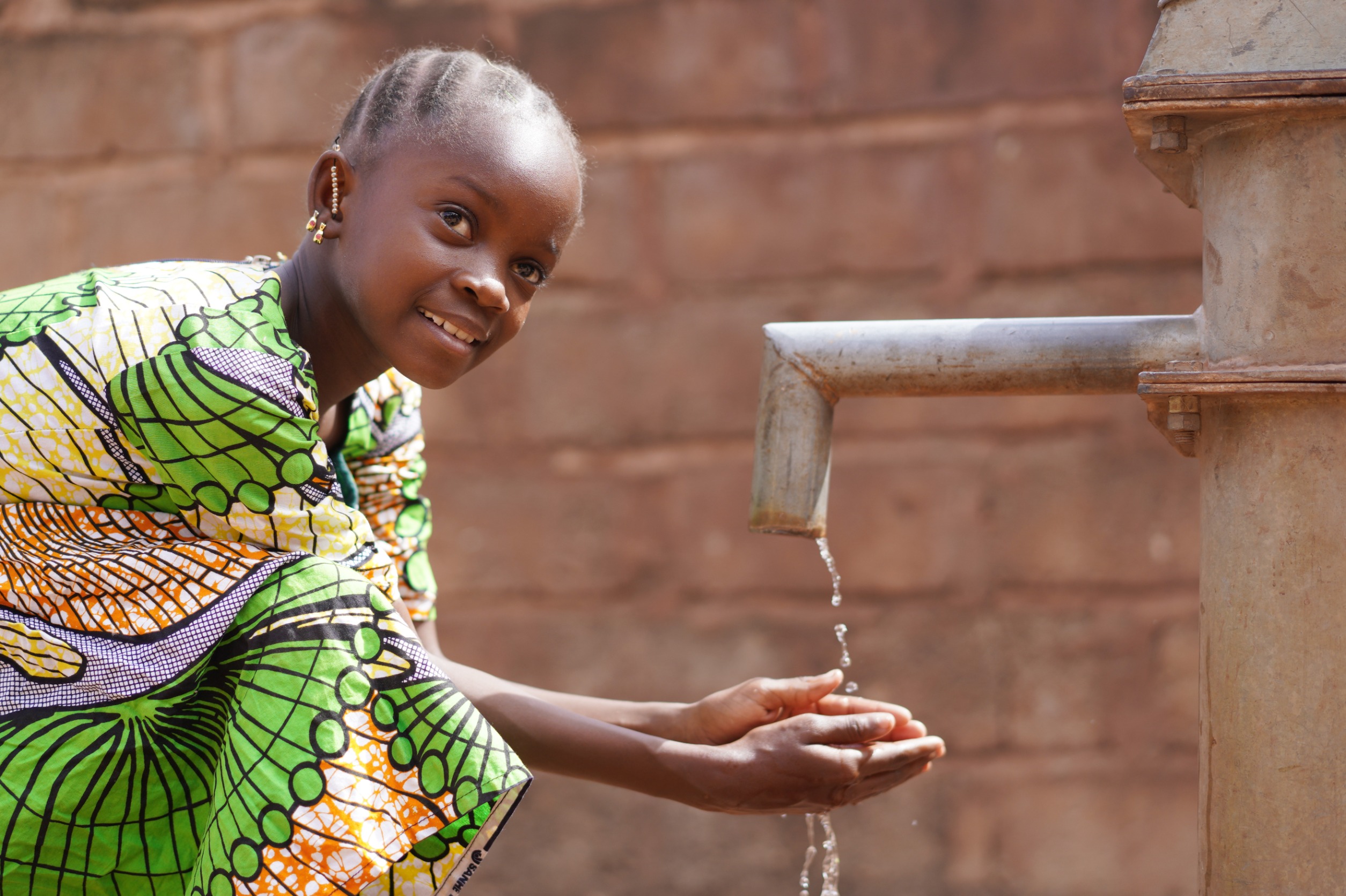 girl child reaching out for water with a smile on her face